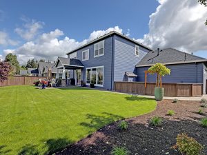 A photo capturing the back of a large blue home with its expansive green yard.